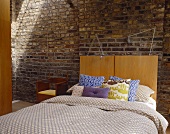 Double bed with wood headboard in front of a brick wall