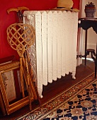 A carpet beater and a picture frame next to an antique radiator against a red wall