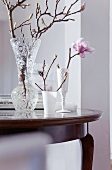 A magnolia sprig in a glass vase on an antique table
