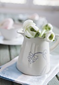 White peonies in a white pitcher with decorative painting on a dish towel