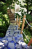 Blaue Mosaiktreppe führt zwischen Bäumen zum Haus