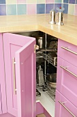 Salz und Pfeffermühle auf Arbeitsplatte über offenem Küchendrehschrank mit rosa Holzfront