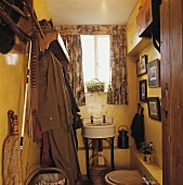 Gelber Toilettenraum mit antikem Waschbecken, einer Toilette, einer Garderobe mit Mäntel und einer Angelausrüstung