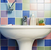 Nahaufnahme von Toilettenartikeln auf einem weißen Waschbecken, rundherum bunte, pastellfarbene Wandfliesen