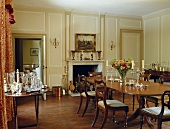 Esszimmer mit cremefarbener Vertäfelung, einem Holzboden, Regency-Esstisch und Stühle und Karaffen und Gläser auf einem Beistelltisch