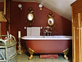 Terrakottafarbenes Dachgeschoss mit Clawfoot-Badewanne und darüberhängenden, ovalen Spiegeln mit üppigem Goldrahmen