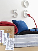 A bedroom with blue cushions on the bed, numbers as wall decoration and a red table lamp