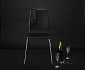A glove over the back of a black chair with champagne and precious stone next to it
