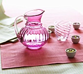 A pink carafe, a glass and small candles in bowls as table decoration