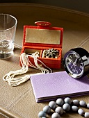 A necklace in a jewellery box, an alarm clock, a diary and a glass on a leather-covered tray