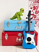 A red suitcase and a blue suitcase, a toy guitar and an stuffed animal