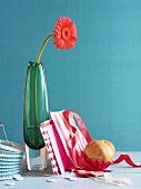 A gerbera in a green vase, paper decoration and a brioche
