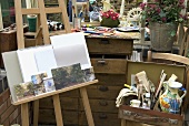 Bilder auf Staffelei neben einem alten Koffer mit Farben & Pinseln im Künstler-Studio im Gartenhaus