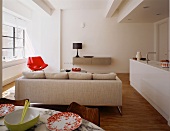 An open-plan designer living room with a view of the back of a natural coloured sofa in front of a white kitchen counter