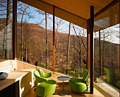 Green designer armchairs in the corner of a living room in front of a glazed facade with a view