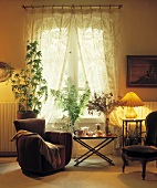 Brauner Sessel, Beistelltisch und Zimmerpflanzen vor dem Fenster mit cremefarbenem Vorhang