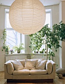Grosse Lampe mit Papierlampenschirm im Wohnzimmer mit Sofa und Zimmerpflanzen