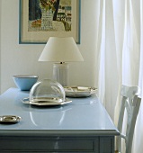 Glas-Cloche und weiße Lampe auf pastellblauem Tisch