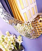 Moderner Spiegel an lila getönter Wand über Blumen im Topf