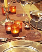 Brennende Windlichter neben gefülltem Weinglas und Silberbesteck mit Silbertellern