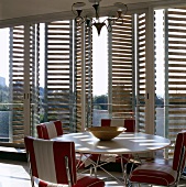 A round table and chairs in front of terrace windows with wooden shutters