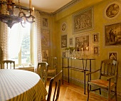 Brennende Kerzen auf Glaskonsole mit Metallgestell in Esszimmer mit Bildern im Stil historischer Stiche auf lindgrüner Wand