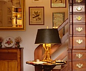 Schubladenschrank im antiken Stil neben brennender Lampe auf kleinem Tisch in traditionellem Wohnzimmer