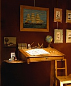 Antikes Schreibpult mit Globus an rotbrauner Wand mit Segelschiffgemälde und Tierzeichnungen