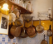 Alte Metallsiebe, Kupferpfannen und altes Emailleschild an Wand über blau-weissen Fliesen in französischer Küche