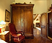 Grosser, antiker Schrank und roter Polstersessel in altem Landhaus-Wohnzimmer mit Fliesenboden