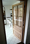 Halbverglaste, offene Holztür in traditionellem Bad mit weissen, diagonal verlegten Fliesen und Säulenwaschbecken