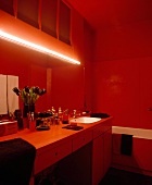 In Rot getauchtes Bad mit Leuchtröhre über langem Schmink- und Waschtisch mit dunklen Tulpen