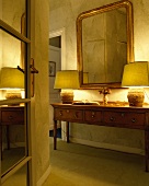 Blick durch offene Spiegeltür auf goldgerahmten Wandspiegel und brennende Lampen auf antiker Kiefern-Konsole