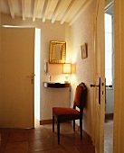 Antiker, rotbraun gepolsterter Stuhl neben goldgerahmtem Spiegel und brennender Lampe zwischen leicht geöffneten Türen