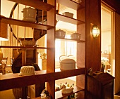 Offenes Raumteilerregal aus Holz mit weisser Porzellandekoration und Durchblick auf Wendeltreppe in traditionellem Wohnraum