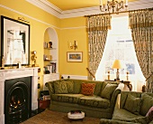 Gemusterte Vorhänge und grüne Polstersofas neben Kamin in gelbem, traditionellem Wohnzimmer