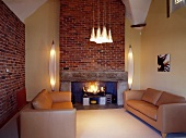 Wohnzimmer in Karamelltönen mit moderner Beleuchtung und brennendem Kamin in Backsteinmauer