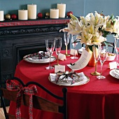Für Weihnachtsessen gedeckter Tisch mit weissen Lilien auf rotem Tischtuch und Schottenkaro-Bändern in blauem Esszimmer