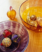 Farbige Glasschalen auf Holztisch mit Christbaumkugeln in Lila, Rot und Gold