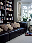 Schwarzbraune Ledercouch mit naturfarbenen Kissen vor dunklen Bücherregalen in modernem Wohnzimmer