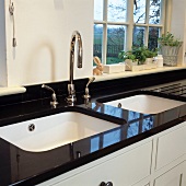Weisses Doppelspülbecken mit modernem Wasserhahn in schwarzer Granitarbeitsplatte vor Sprossenfenster in moderner Küche