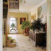 Fliesenboden und antike geschnitzte Truhe in großem, hellem Eingangsbereich mit Zimmerpflanzen und Bildern