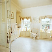 Cremefarbene Schabraken, Jalousien und Büsten an Fenstern auf beiden Seiten der Toilette in traditionellem Bad