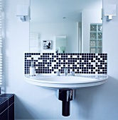 Modernes Waschbecken mit schmalem Band aus schwarzen und weissen Mosaikfliesen unter Spiegel mit kubischen Lämpchen