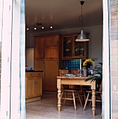 Blick durch offene Tür in traditionelle Holzküche mit rustikalem Tisch und Stühlen aus Kiefer