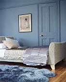 Seidendecken auf einem gepolstertem Bett in einem blauen Zimmer mit blauem Kunstfell-Teppich auf dem Parkett