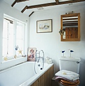 Holzrahmenspiegel über der Toilette und eine Badewanne mit Holzvertäfelung in einem weissen Badezimmer