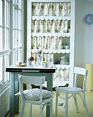 weiße Stühle, ein kleiner Tisch mit Zinkplatte und ein Regal mit Vorhängen in einem Esszimmer mit gelbem Boden