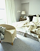 Pelzdecke und Kissen auf dem Bett und ein Sessel mit Wildlederbezug in einem Schlafzimmer mit grauem Teppich