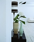 Eine Tischlampe mit schwarz-weißem Schirm neben einer Vase mit Hortensie